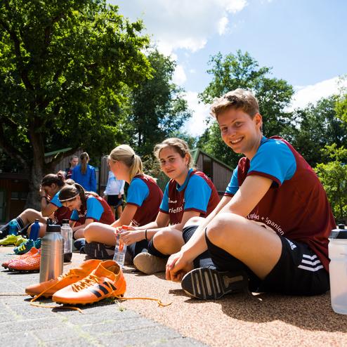 M&auml;dchenmannschaft sitzt auf dem Boden, w&auml;hrend sie Fu&szlig;ballschuhe anziehen und sich auf das Training vorbereiten.