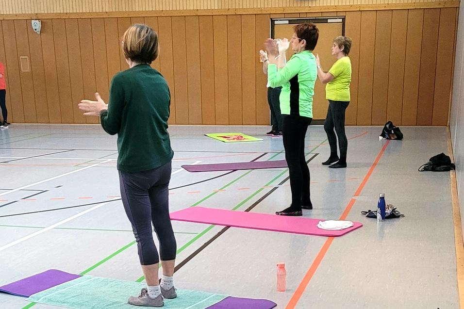 Gruppentraining in einer Halle, mit Teilnehmern auf Matten, die aktiv &Uuml;bungen durchf&uuml;hren und applaudieren.