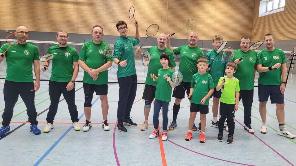 Gruppensfoto von zehn Badmintonspielern in grünen T-Shirts, die Schläger in einer Sporthalle halten.