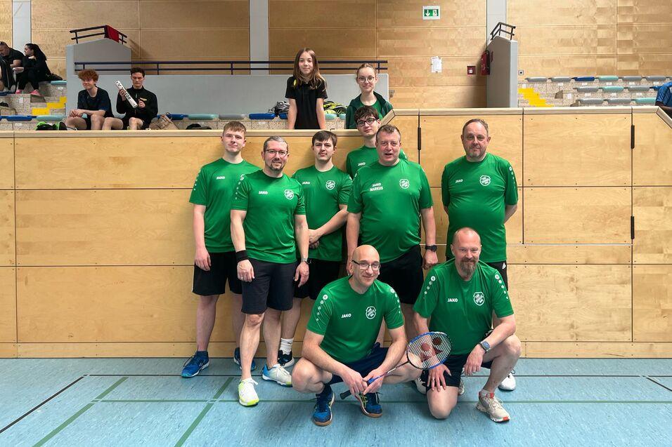 Gruppenfoto von acht Basketballspielern in gr&uuml;nen Trikots, die vor einer Sporthalle posieren.