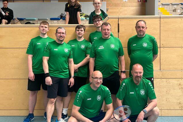 Gruppenfoto von acht Basketballspielern in gr&uuml;nen Trikots, die vor einer Sporthalle posieren.