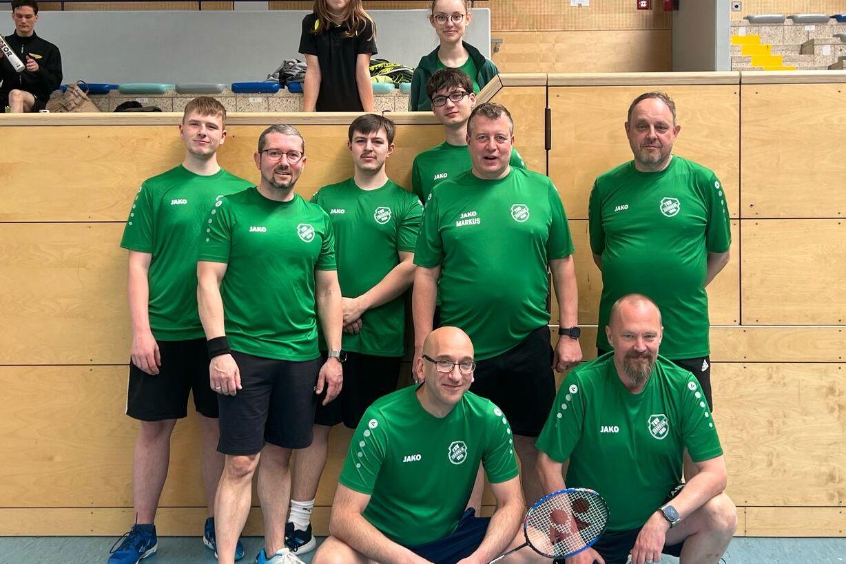 Gruppenfoto von acht Basketballspielern in grünen Trikots, die vor einer Sporthalle posieren.