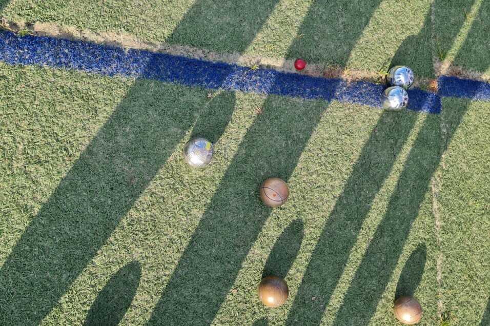 Blick von oben auf einen Rasenplatz mit Kugeln in verschiedenen Farben und langen Schatten von Spielern.