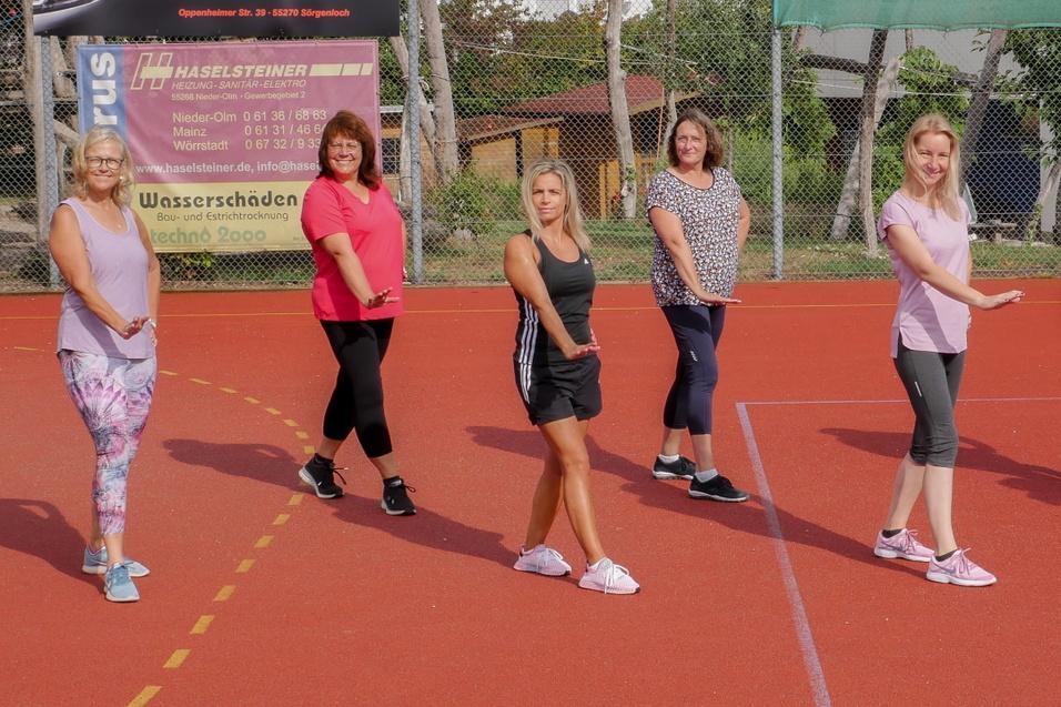 Gruppenszene von sieben Frauen in Sportkleidung auf einem roten Sportplatz in Bewegung.