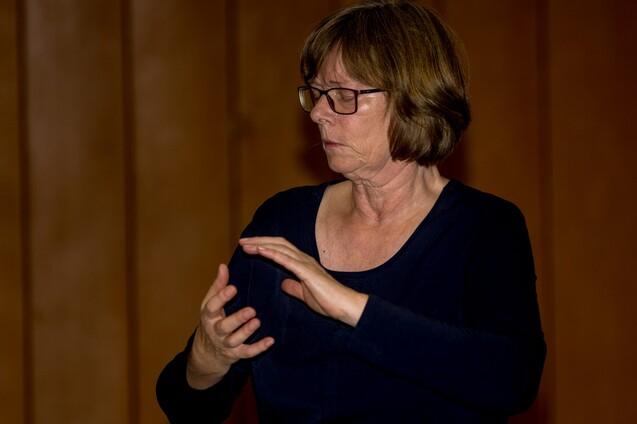 Frau mit Brille f&uuml;hrt eine Handbewegung in einem Sportraum mit Holzverkleidung aus.