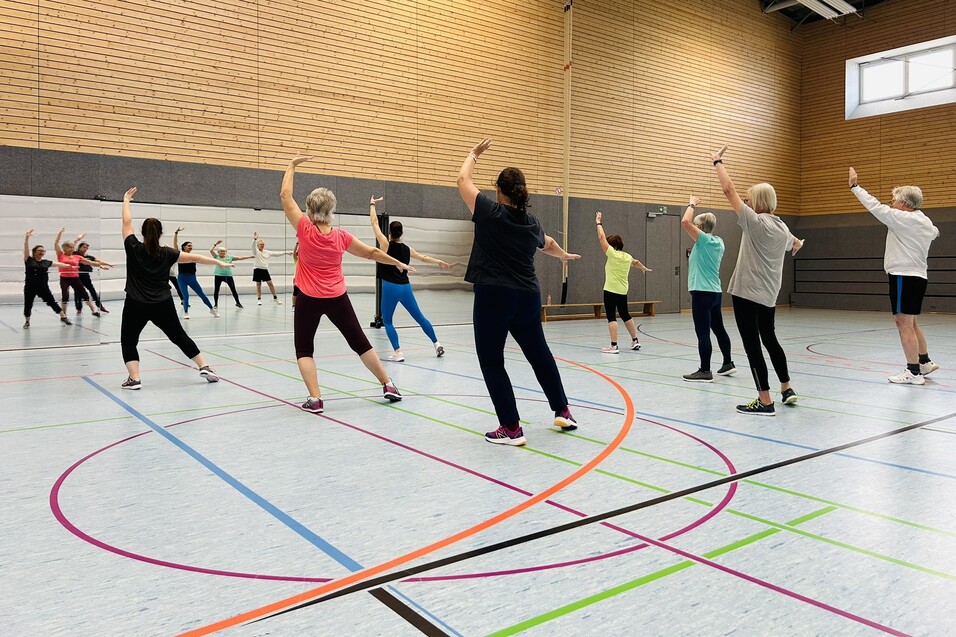 Gruppe von Frauen in Sportkleidung, die synchron Aerobic-&Uuml;bungen in einer Turnhalle ausf&uuml;hren.