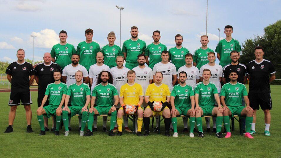Gruppenfoto einer Fu&szlig;ballmannschaft in gr&uuml;nen Trikots, auf dem Rasenfeld mit zwei Torwarten in gelben Trikots.