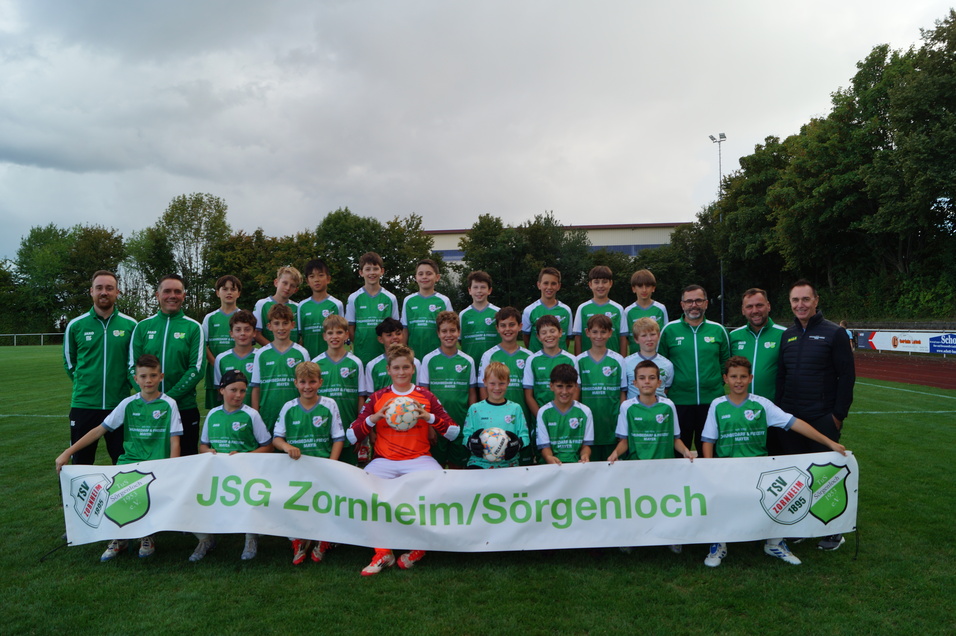 Mannschaftsfoto der JSG Zornheim/S&ouml;rgenloch mit 30 Spielern und Trainern auf einem Fu&szlig;ballplatz, Banner im Vordergrund.
