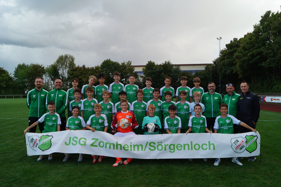 Gruppenfoto von Spielern der JSG Zornheim/S&ouml;rgenloch in gr&uuml;nen Trikots auf einem Fu&szlig;ballplatz mit Banner.