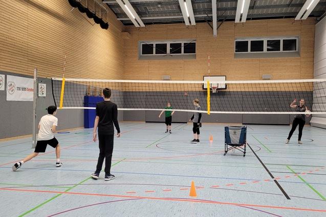 Eine Gruppe von f&uuml;nf Personen spielt Volleyball in einer Sporthalle mit Linien und Netzen.