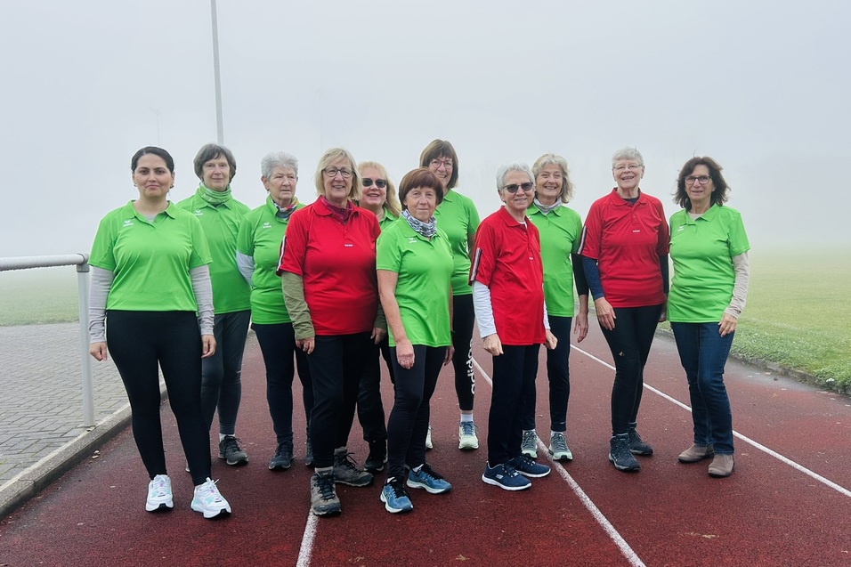Gruppe von zehn Frauen in gr&uuml;nen und roten Sportshirts auf einer Laufbahn im Nebel.