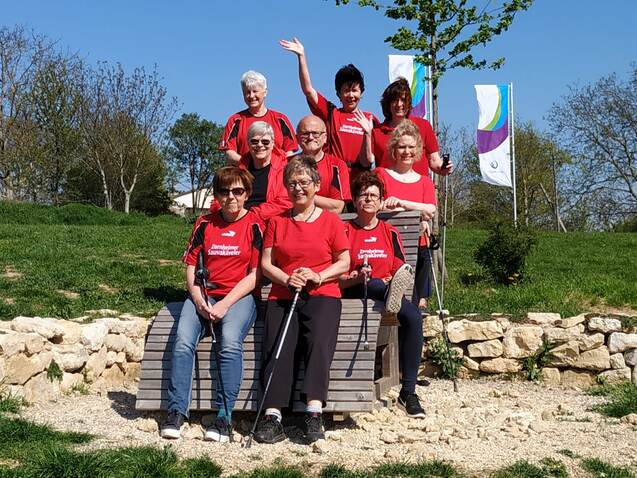 Gruppe von acht Personen in roten T-Shirts sitzt und steht auf einem Holzgestell in einem Park mit grüner Wiese.