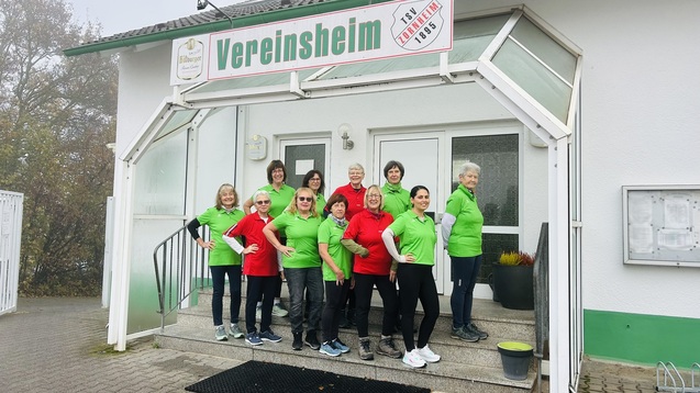 Gruppe von zehn Frauen in bunten T-Shirts vor dem Vereinsheim, das mit einem Schild versehen ist.