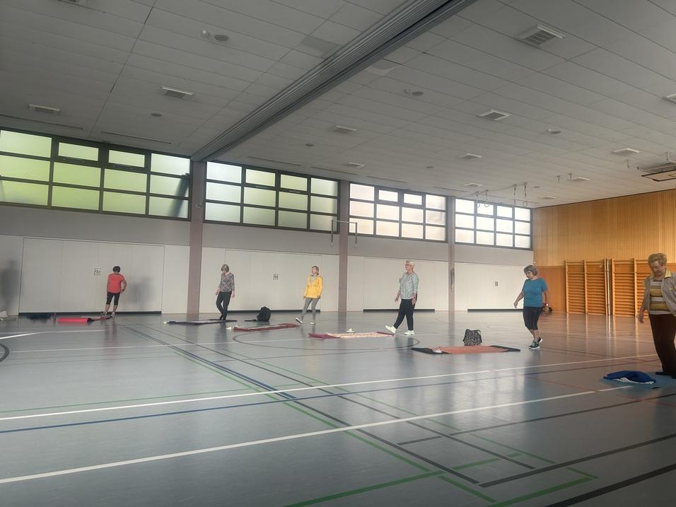 Gruppentraining in einer Sporthalle mit mehreren Menschen, die auf Matten &Uuml;bungen durchf&uuml;hren.