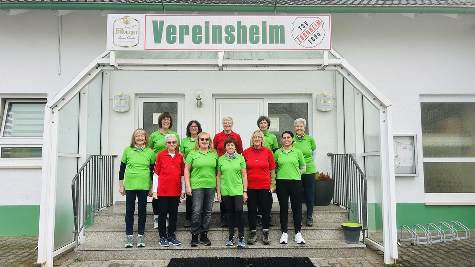 Gruppe von Frauen in roten und gr&uuml;nen T-Shirts vor dem Vereinsheim, beschriftet mit "Vereinsheim".