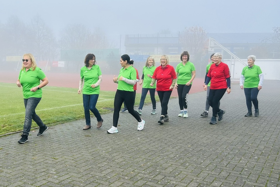 Gruppe von Frauen in gr&uuml;nen und roten T-Shirts joggt im Nebel auf einem Sportgel&auml;nde.