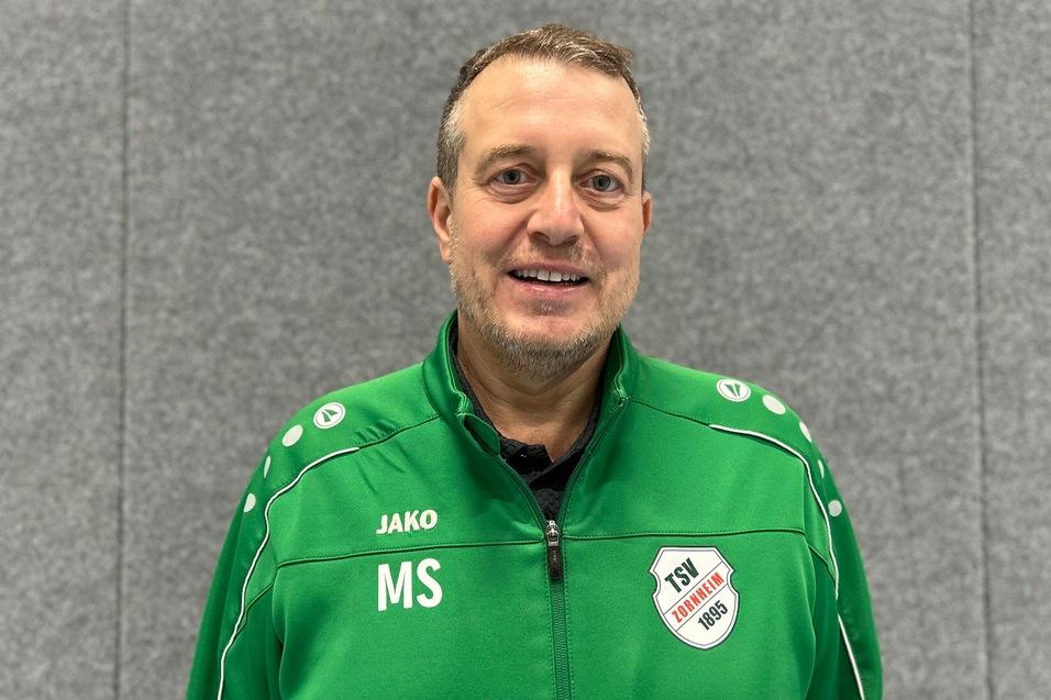 Ein Mann in einem gr&uuml;nen Sportjacke mit dem Schriftzug "TSV" und Initialen "MS" steht vor einem grauen Hintergrund.