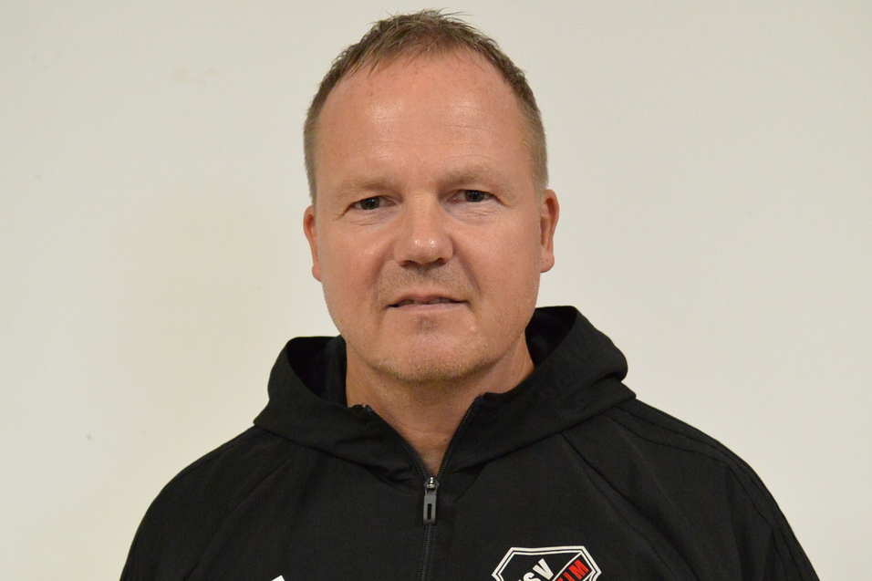 Portr&auml;t eines Mannes in schwarz-wei&szlig;er Sportjacke mit Logo des TSV 1895, vor einem wei&szlig;en Hintergrund.