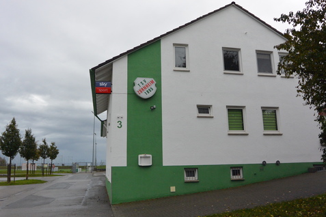Eckgeb&auml;ude mit gr&uuml;nem Sockel und einem Schild des Sky-Sportangebots an der Fassade. Wolkiger Himmel im Hintergrund.