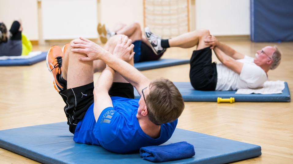Gruppe von Personen bei Bauchmuskelübungen auf Trainingsmatten in einem Fitnessraum.