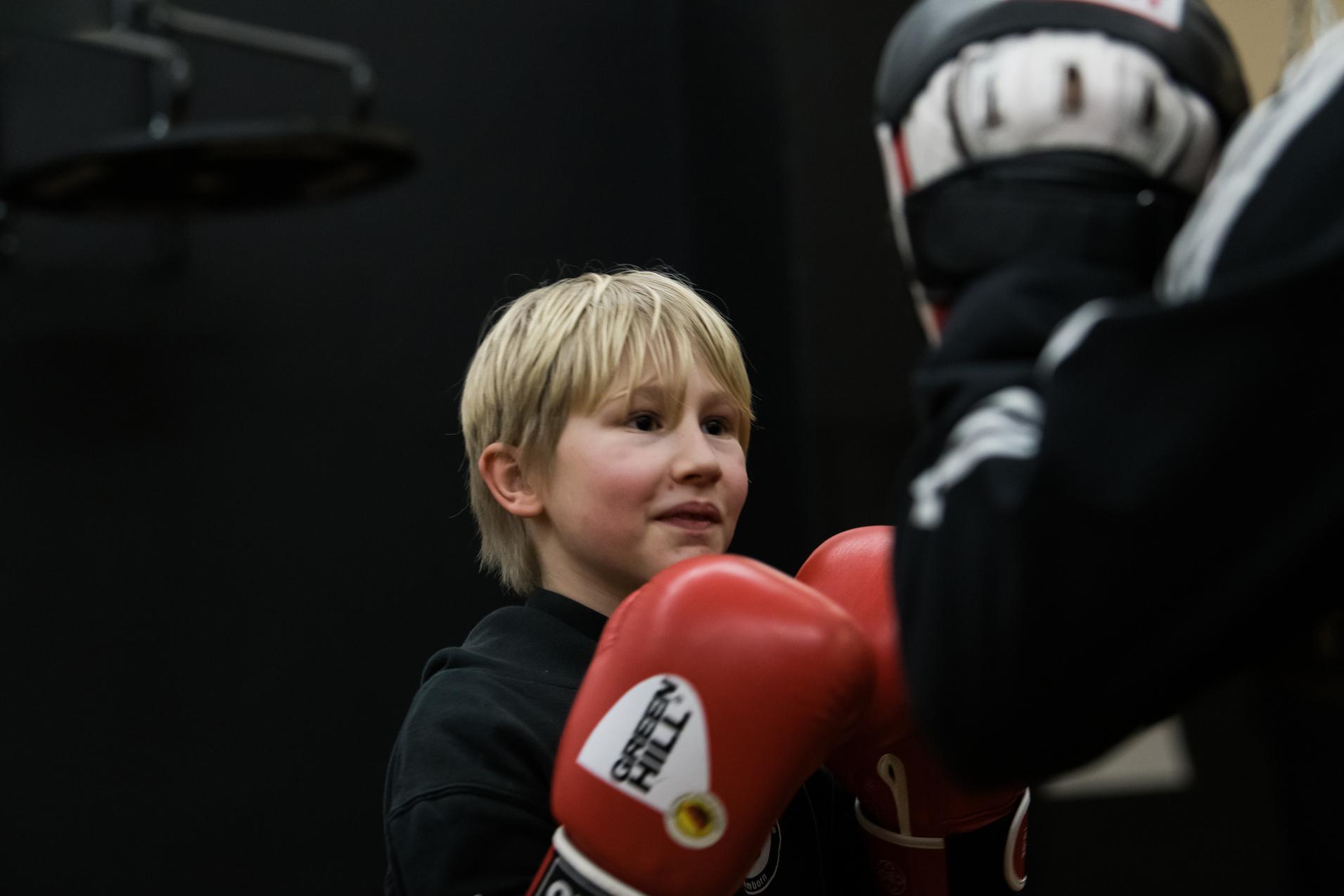 Junger Boxer mit blondem Haar trÀgt rote Handschuhe und lÀchelt wÀhrend des Trainings in einem Sportstudio.