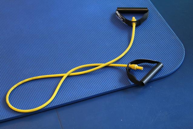 Gelbes Widerstandsband mit schwarzen Griffen auf einer blauen Gymnastikmatte.